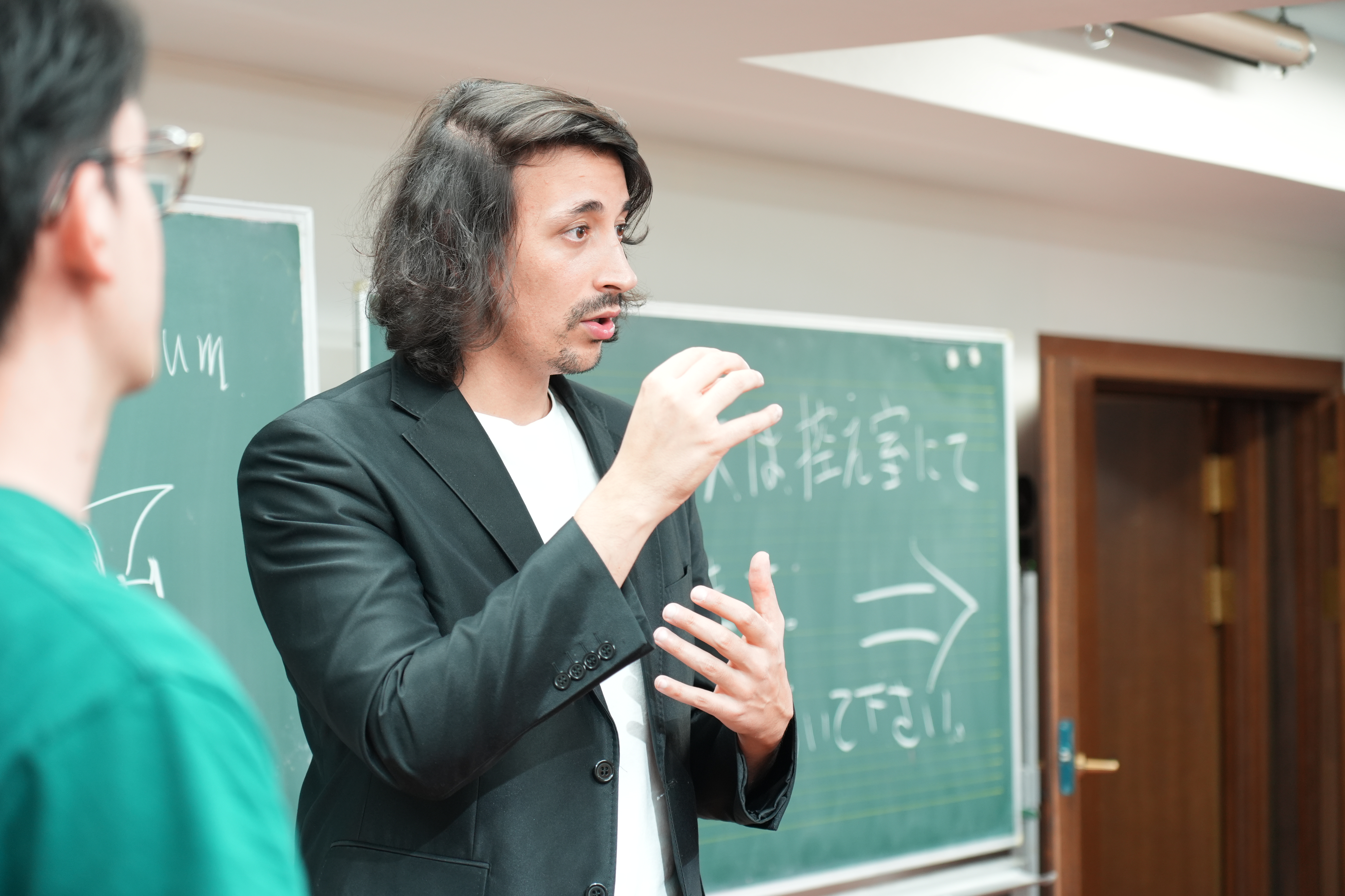 黒板の前で、両手を使って身振りを交えながら説明する講師。